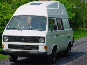 Witte VW T3 camper met hoogdak en fietsen achterop op de weg