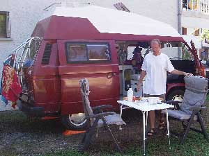Rode VW T3 camper met persoon bij uitgestalde tuinmeubelen