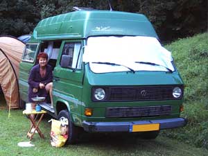 Groene VW T3 Syncro camper met verhoogd dak zonnewering over de voorruit en vrouw in de schuifdeur