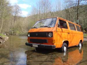 Oranje T3 kombi geparkeerd in een rivier met laag water