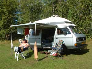 Camper met luifel en kampeermeubelen en zonnebadende persoon