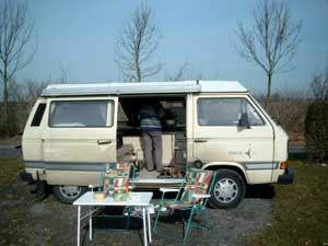 T3 camper met geopende schuifdeur en kampeertafel met stoelen